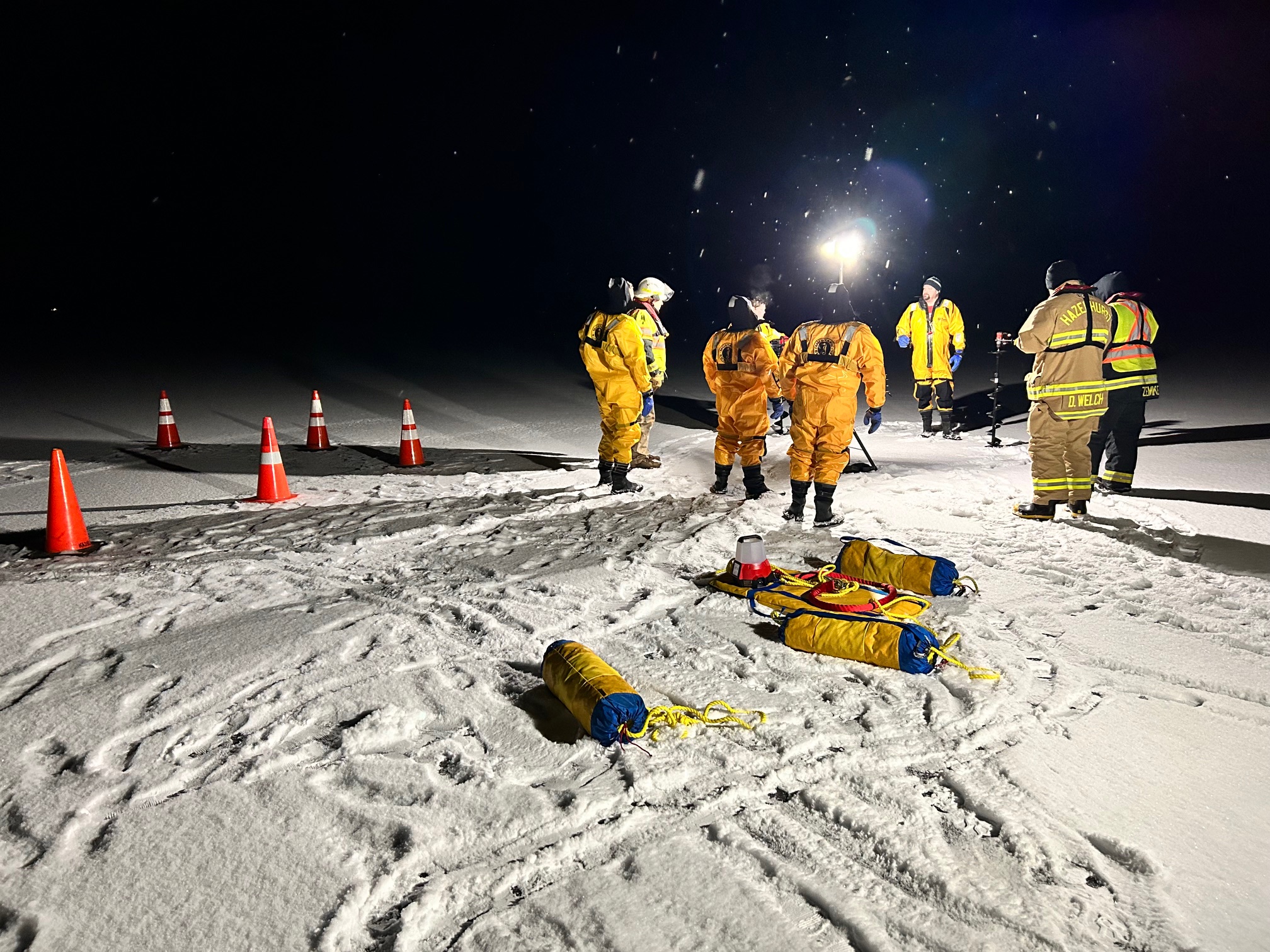 Responders training with ice-rescue equipment on a snow-covered lake during the day